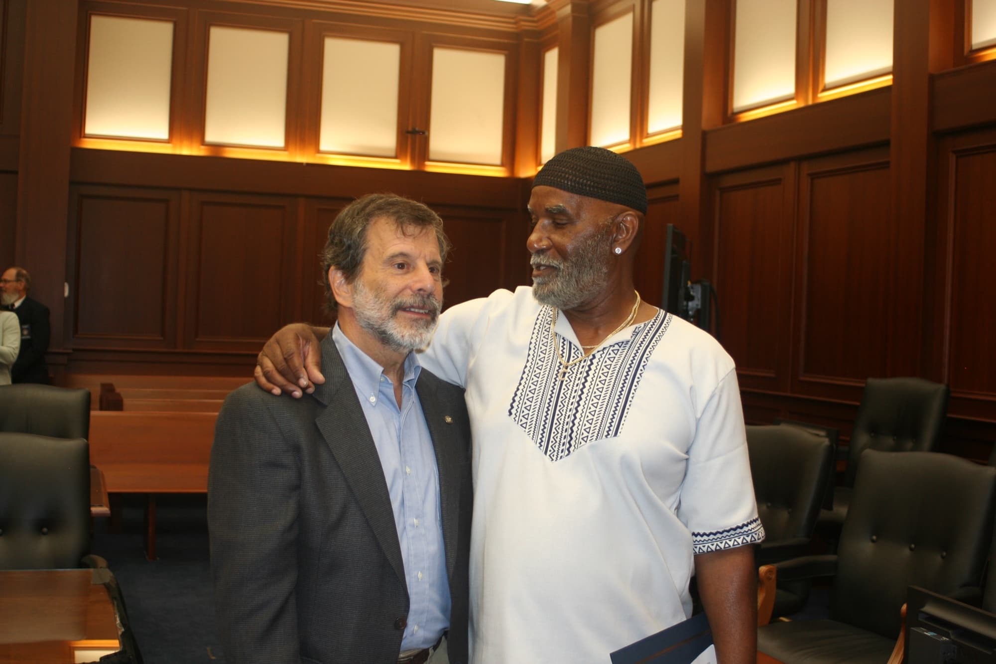 A graduate and court team member standing together in the courtroom