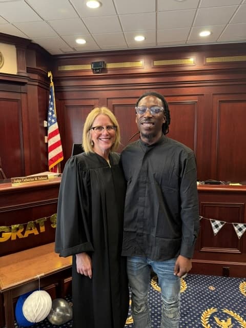 A graduate standing with a judge in a decorated courtroom